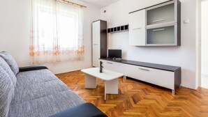 Un espace de vie compact comprenant un canapé, une petite table blanche, un téléviseur et un meuble avec des tiroirs.