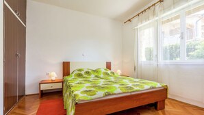 Une chambre à coucher avec un lit en bois, une table de chevet, un tapis rouge et une fenêtre avec des rideaux.