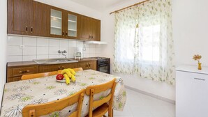 Une cuisine avec des meubles en bois, une table à manger avec des chaises, un réfrigérateur et une fenêtre agrémentée de rideaux à motifs floraux.