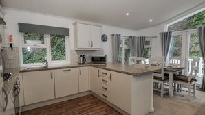 A modern kitchen with white cabinets, a wooden floor, and a dining area with a table and chairs. - Seacroft (Narberth)