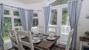 A dining area with a table set for four, white chairs, and a view of a white fence and greenery outside. - Seacroft (Narberth)
