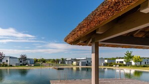 Moderni ulkouima-allasalue, jossa on puinen terassi, kirkas vesi ja olkikatteinen huvimaja.