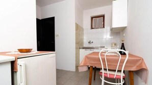 A compact kitchen with white cabinets, a small dining table with a pink tablecloth, and a white chair. - Apartment Dalmatin Zuljana - Two-bedroom Apartment 2 (Ston)