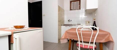 A compact kitchen with white cabinets, a small dining table with a pink tablecloth, and a white chair.