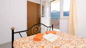 A bedroom with a bed, a window with a view of mountains, and a wooden door. - Apartment Dalmatin Zuljana - Two-bedroom Apartment 2 (Ston)