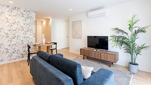 Una sala de estar moderna con un sofá, televisión y un comedor con mesa y sillas.