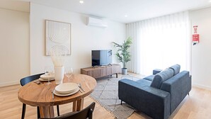 Una sala moderna con una mesa de comedor de madera, un sofá gris y un televisor de pantalla plana.