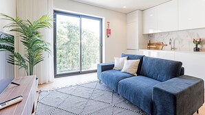 Una sala de estar moderna con un sofá azul, un ventanal grande y una zona de cocina.