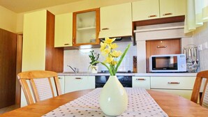 A modern kitchen with white cabinets, a microwave, and a vase with yellow flowers on the dining table. - Apartments Sea Line - Two Bedroom Apartment With Terrace and Sea View (Blato)