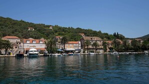 A coastal town with buildings on a hillside, boats docked along the shore, and palm trees.