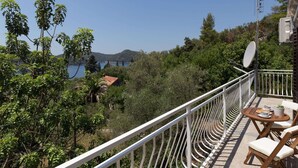 A balcony with a view of a coastal landscape, including trees and a body of water.