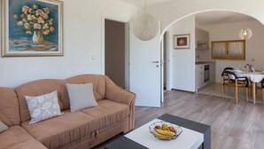 A living room with a sofa, a dining table with chairs, and a kitchen visible through an archway.