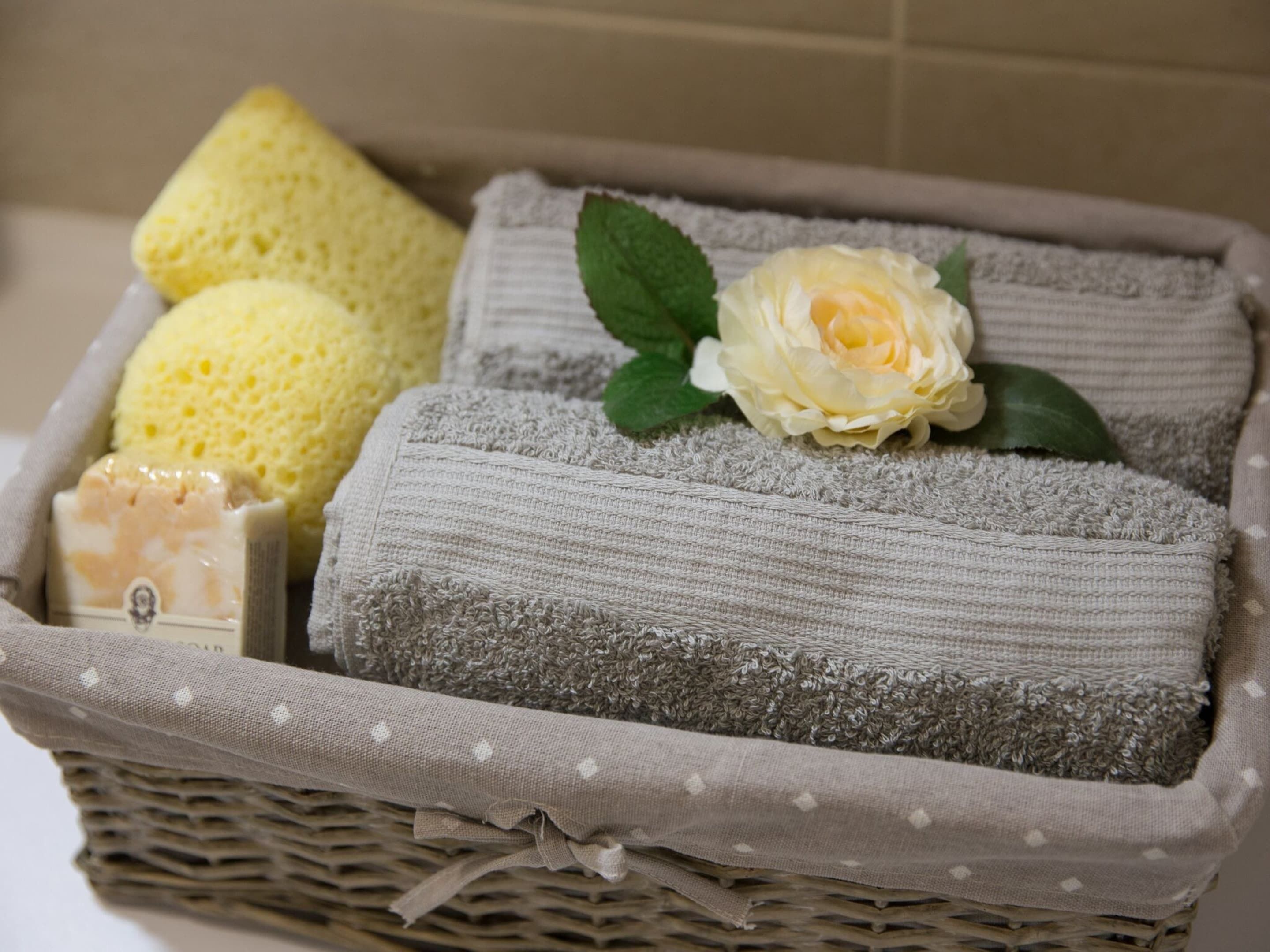 A wicker basket containing folded towels, a yellow sponge, and a bar of soap.