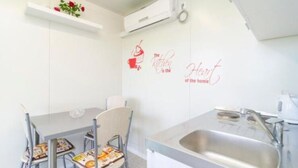 Une cuisine moderne avec des murs blancs, un évier en acier inoxydable et un coin repas comprenant deux chaises et une table.