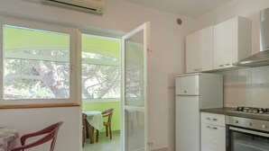 A compact kitchen with a refrigerator, stove, and oven. A dining area with a table and chairs is visible through an open door. - Seafront Apartments Olivera-standard One Bedroom Apartment With Balcony and Sea View (Blato)