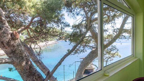 A room with a large window overlooking a coastal area with trees and a beach. - Seafront Apartments Olivera-standard One Bedroom Apartment With Balcony and Sea View (Blato)