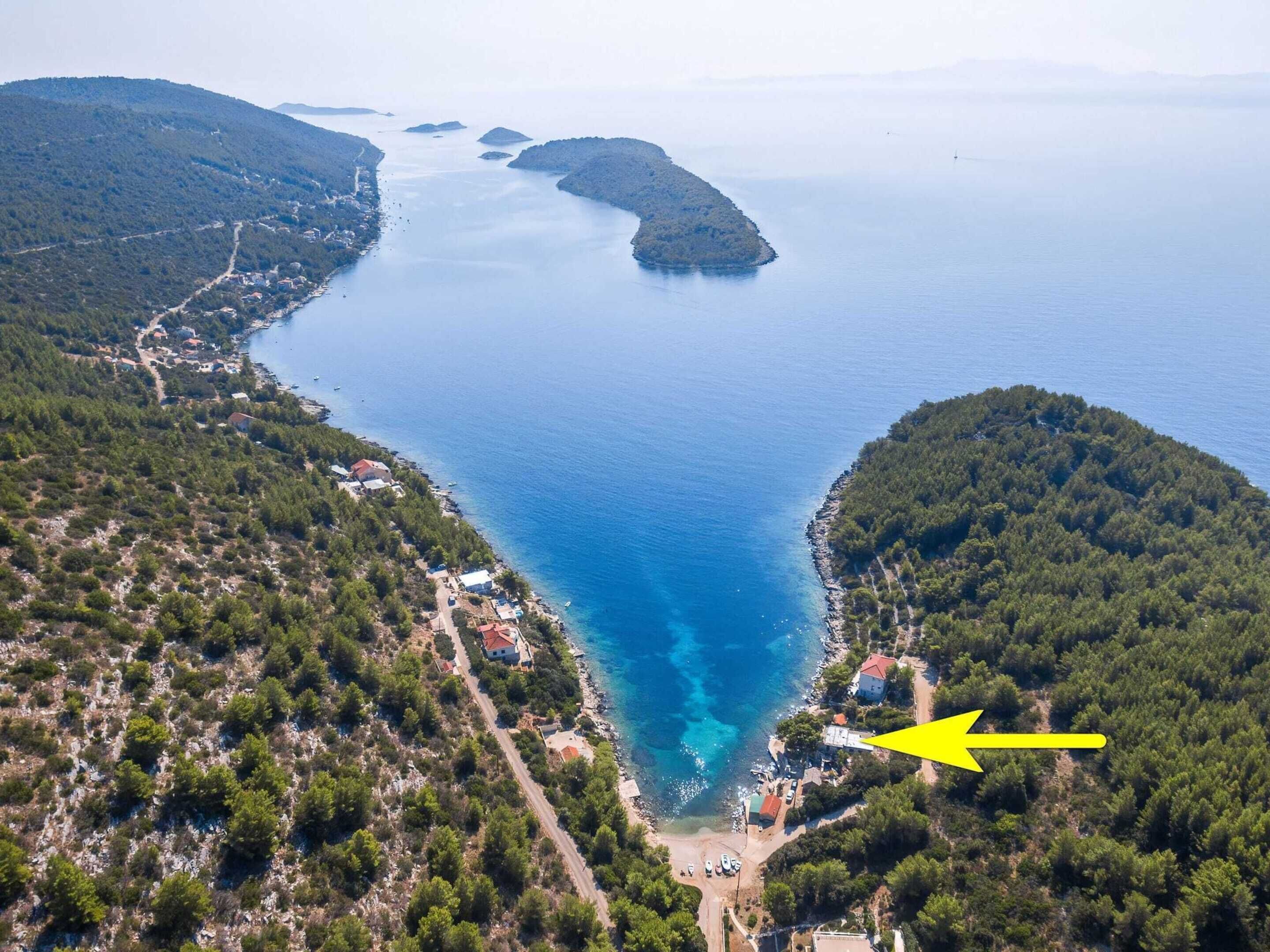 Luchtbeeld van een kustgebied met een klein strand, omringd door beboste heuvels.