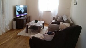Ein Wohnzimmer mit Fernseher, einer Couch, einem Couchtisch und einem Fenster mit Vorhängen.