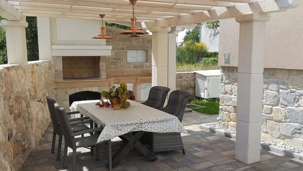 Eine Terrassengaststätte mit Kamin aus Stein, Korbstühlen und einem Tisch mit weißem Tuch.