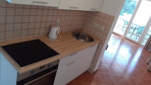 A compact kitchen with a stove, oven, sink, and a kettle on the countertop.