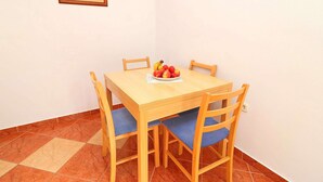 A small dining area with a wooden table and four chairs, each with a blue cushion. A bowl of fruit is placed on the table.