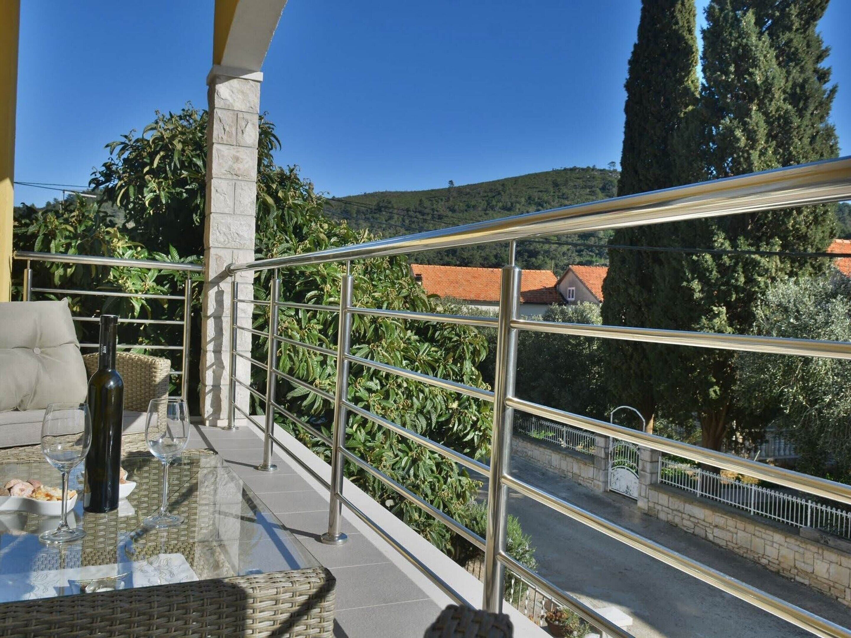 Un balcon doté d’une table en verre, d’une rambarde en métal et offrant une vue sur un immeuble aux toits rouges et sur des arbres.