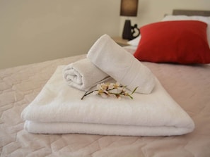 A neatly folded white towel on a bed with a red pillow and a small branch with white flowers.