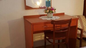 A wooden desk with a chair, a vase of flowers, and a mirror on the wall.