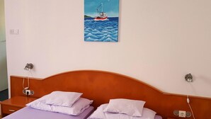 A double bed with two pillows, a wooden headboard, and a wall-mounted painting of a boat on water.