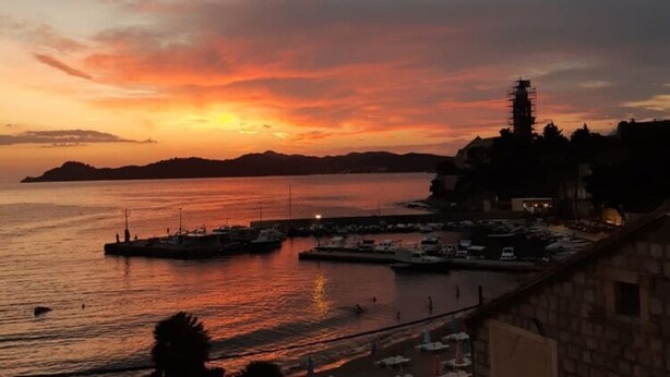 A coastal sunset view with a marina, boats, and a distant island.