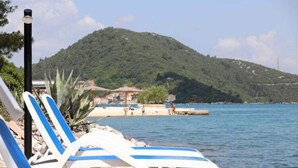 A beachside view with lounge chairs, a mountain in the background, and a beach area with people. - Apartments More & Ja - Superior One Bedroom Apartment With Terrace and Sea View (Ston)