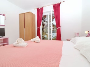 A bedroom with a bed, a TV on a pink stand, a wardrobe, and a window with red curtains. - Apartments More & Ja - Superior One Bedroom Apartment With Terrace and Sea View (Ston)