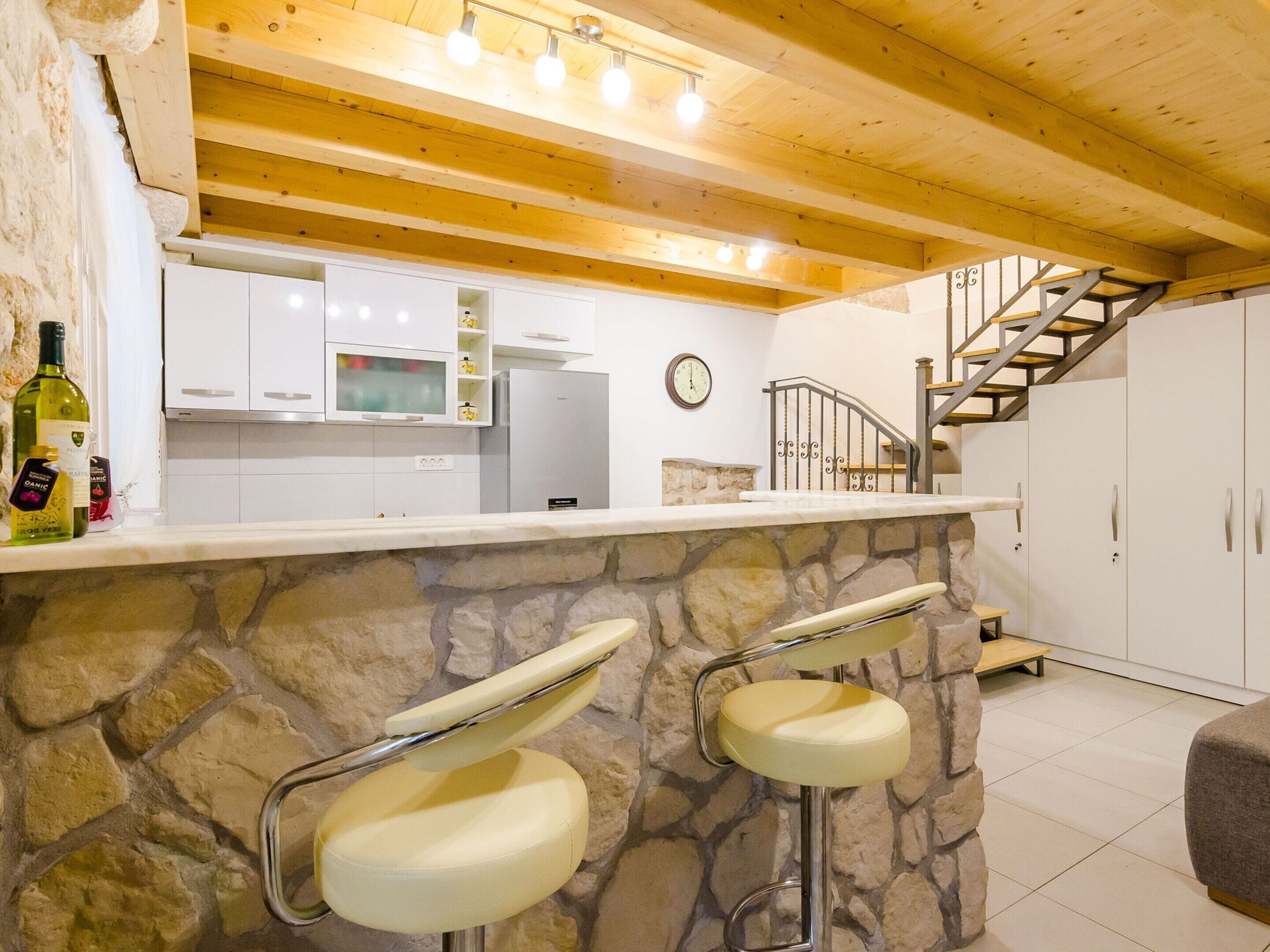 Una cocina con encimeras de piedra, armarios blancos y techo de madera.