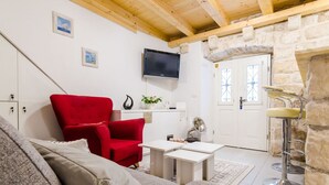 Ein gemütliches Wohnzimmer mit einem roten Sessel, einem grauen Sofa, einem kleinen weißen Tisch und einer Steinwand.