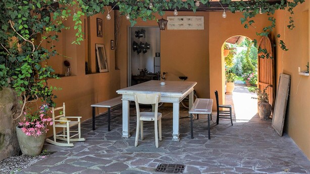Une terrasse dallée de pierres, avec une table et des chaises, entourée de murs orange et de verdure.