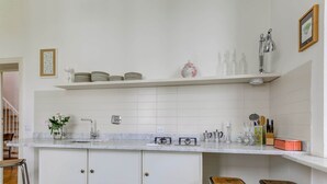 Une cuisine moderne avec des armoires blanches, un comptoir en marbre et un évier en acier inoxydable. On y trouve deux tabourets et une petite étagère contenant des ustensiles de cuisine.