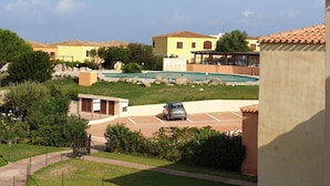 Zona residencial con piscina, un coche aparcado y un edificio de techo con tejas.