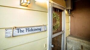 A wooden sign with "The Hideaway" written on it, attached to a building with a window and a door.