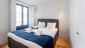 Een moderne slaapkamer met een groot bed, uitzicht op de stad door een schuifdeur en een ontbijtkarretje op het bed.