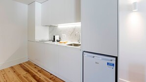 Een kleine keuken met witte kastjes, een marmeren aanrecht, een spoelbak en een inbouwkoelkast.