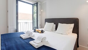 Een hotelkamer met een bed, twee kussens, een dienblad met ontbijtartikelen en een raam met uitzicht op gebouwen.
