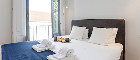 A hotel room with a bed, two pillows, a tray with breakfast items, and a window with a view of buildings.