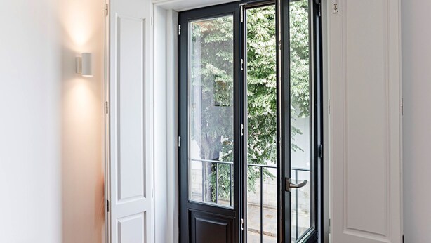 Een deur met een zwart frame, een ruit en een klein balkon met een metalen hekwerk, tegen een witte achtergrond.