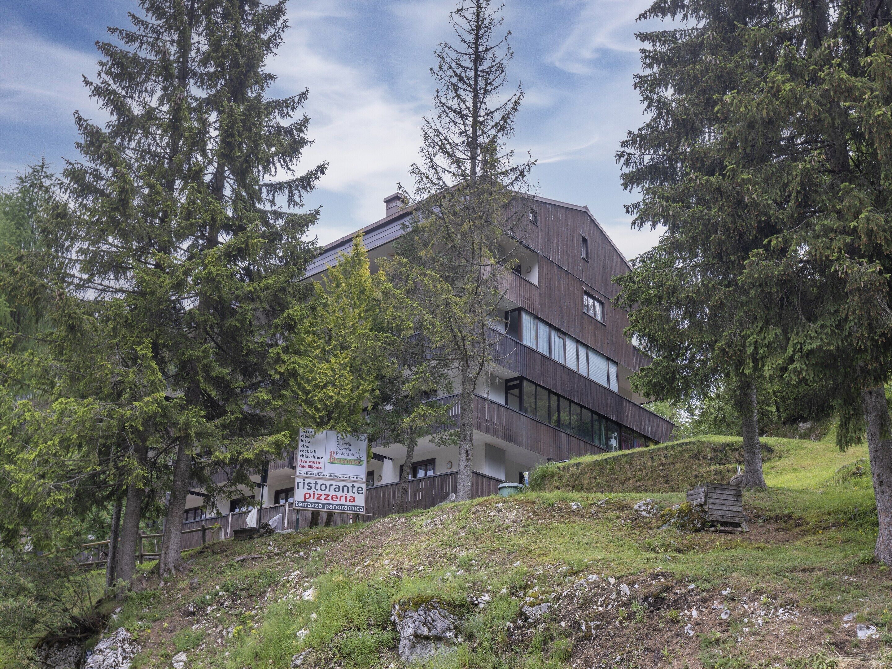 Ein modernes Gebäude mit dunkler Fassade, umgeben von Bäumen und einer grünen Böschung.
