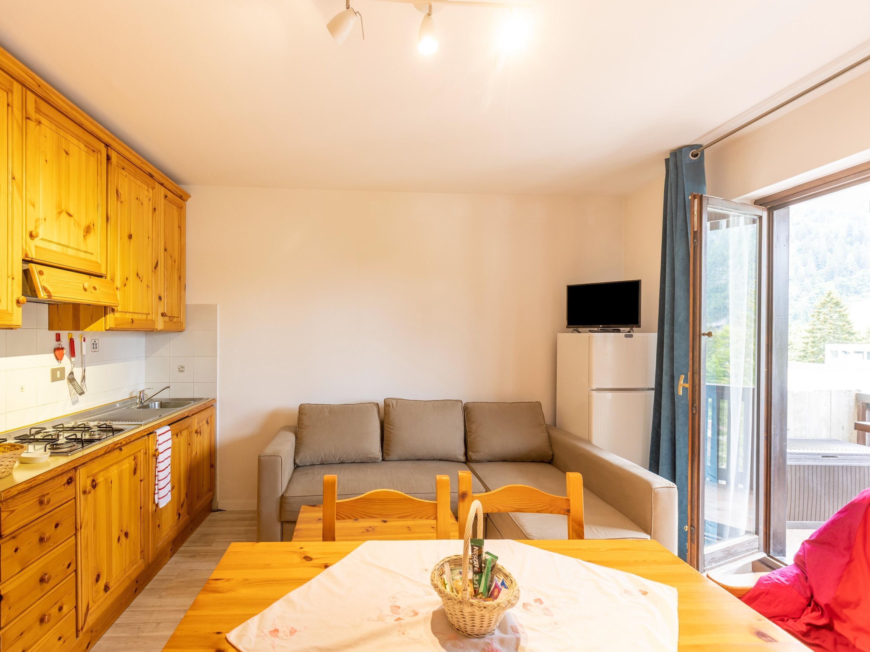 A compact kitchen with wooden cabinets, a dining table with a white tablecloth, and a sofa in the living area.