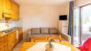 A compact kitchen with wooden cabinets, a dining table with a white tablecloth, and a sofa in the living area. - Apartment in Braulins Near Tagliamento River (Chiusaforte)