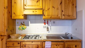 A kitchen with wooden cabinets, a gas stove, a sink, and a tiled backsplash. - Apartment in Braulins Near Tagliamento River (Chiusaforte)
