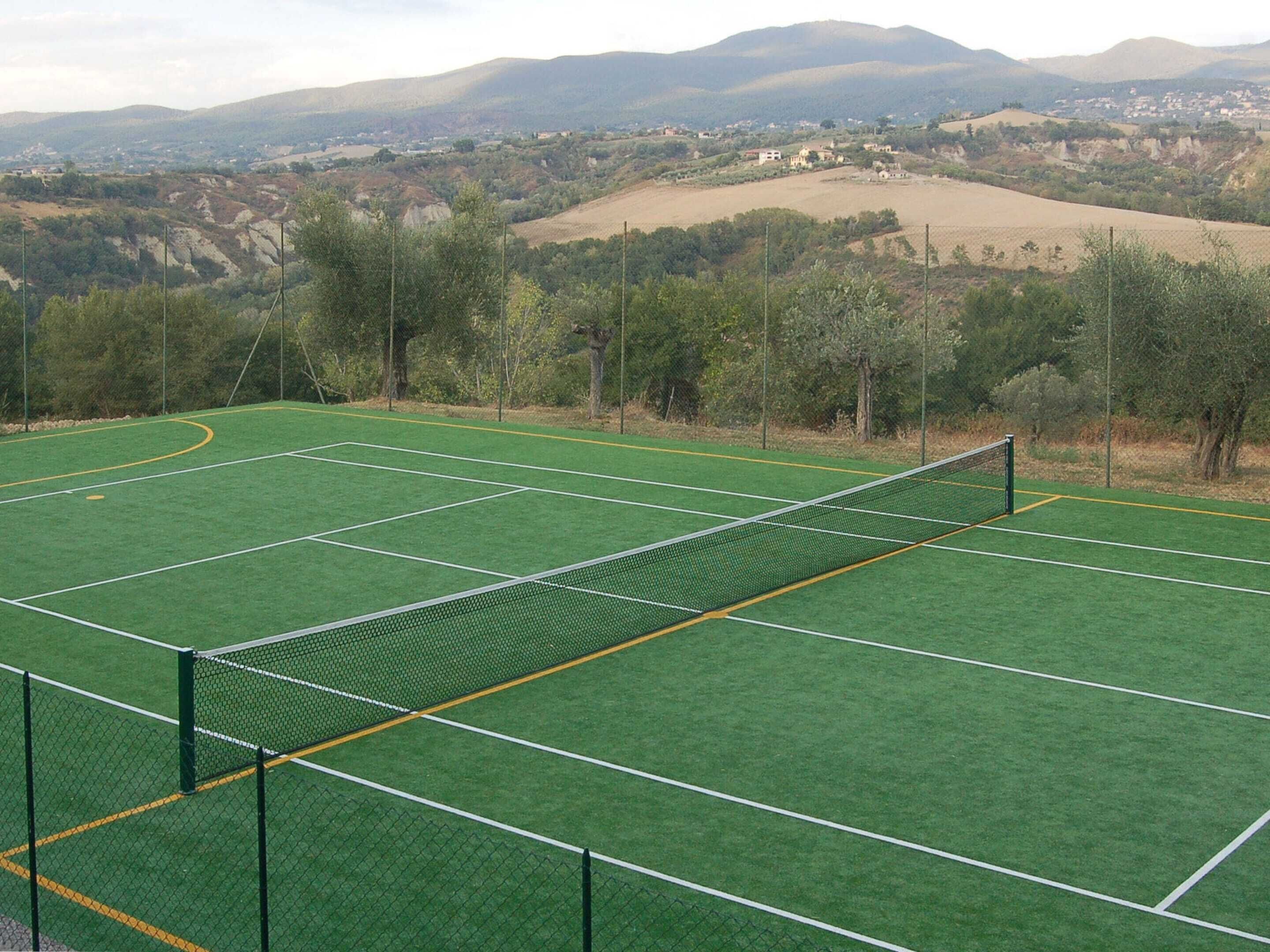 Un court de tennis avec un filet au centre, entouré d’arbres et bordé, au loin, d’un paysage vallonné.