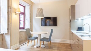 A compact kitchen with a dining area, a TV mounted on the wall, and a window with a red frame. - Oporto Home Wine Cellars - Estúdio Standard - 1ºF (Vila Nova de Gaia)