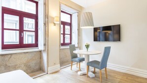 A room with a round table, two chairs, a TV mounted on the wall, and a door with red shutters. - Oporto Home Wine Cellars - Estúdio Standard - 1ºF (Vila Nova de Gaia)